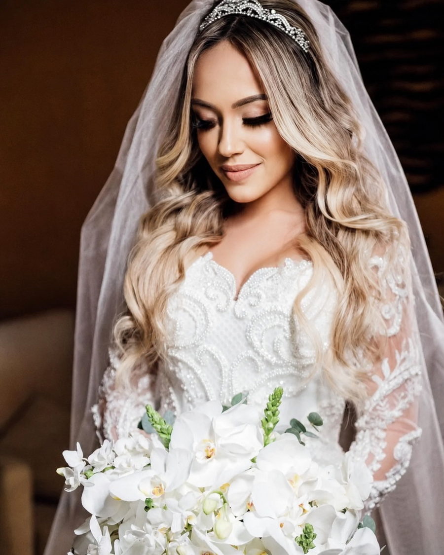 Noiva com véu longo, cabelo solto ondulado e buquê de orquídeas brancas